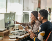 Two office workers looking at charts on a screen