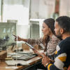 Two office workers looking at charts on a screen